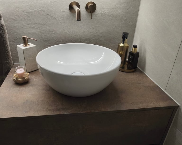 Modern bathroom with round white vessel sink on dark countertop, wall-mounted faucet, and decorative bath accessories